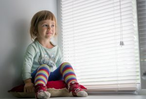 child sat next to venetian blinds
