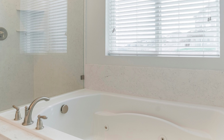 White aluminium blinds in a bathroom with a bath and shower. 