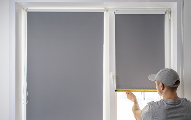 Man installing grey blackout roller blinds