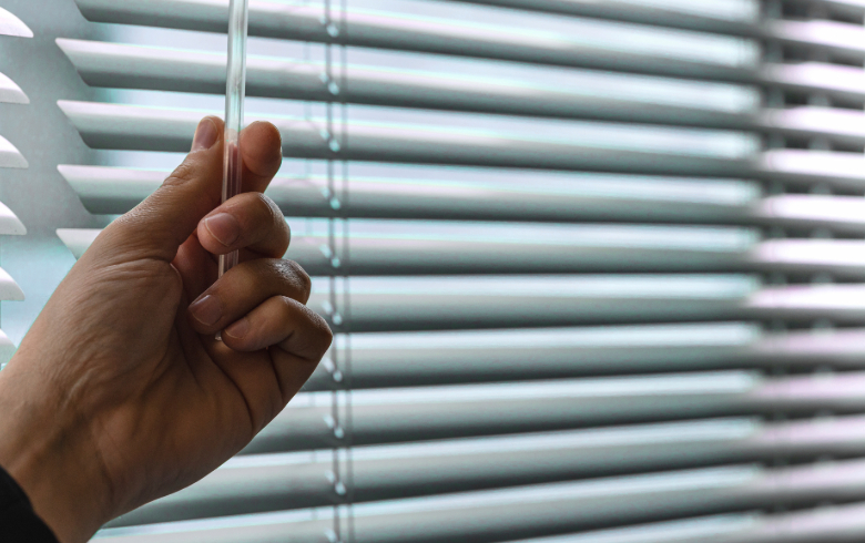 Close-up of an employee's hand adjusting the blinds to control the lighting in an office.